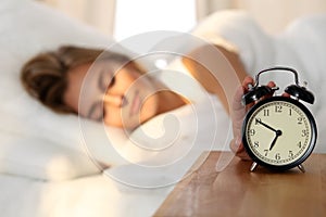 Sleepy young woman stretching hand to ringing alarm willing turn it off. Early wake up, not getting enough sleep