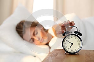 Sleepy young woman stretching hand to ringing alarm willing turn it off. Early wake up, not getting enough sleep