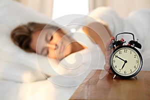 Sleepy young woman stretching hand to ringing alarm willing turn it off. Early wake up, not getting enough sleep