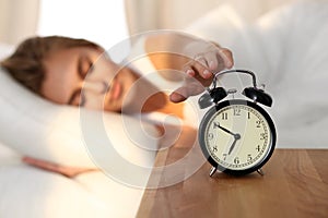 Sleepy young woman stretching hand to ringing alarm willing turn it off. Early wake up, not getting enough sleep