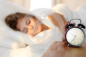 Sleepy young woman stretching hand to ringing alarm willing turn it off. Early wake up, not getting enough sleep