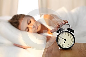 Sleepy young woman stretching hand to ringing alarm willing turn it off. Early wake up, not getting enough sleep