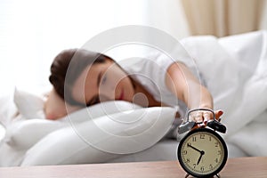 Sleepy young woman stretching hand to ringing alarm willing turn it off. Early wake up, not getting enough sleep