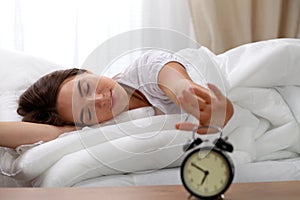 Sleepy young woman stretching hand to ringing alarm willing turn it off. Early wake up, not getting enough sleep