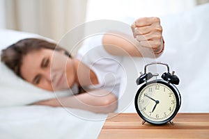 Sleepy young woman stretching hand to ringing alarm willing turn it off. Early wake up, not getting enough sleep concept