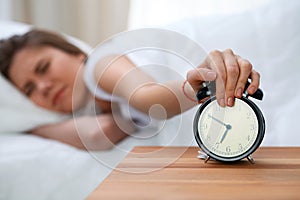 Sleepy young woman stretching hand to ringing alarm willing turn it off. Early wake up, not getting enough sleep concept