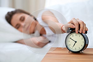 Sleepy young woman stretching hand to ringing alarm willing turn it off. Early wake up, not getting enough sleep concept