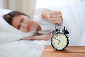 Sleepy young woman stretching hand to ringing alarm willing turn it off. Early wake up, not getting enough sleep concept