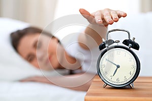 Sleepy young woman stretching hand to ringing alarm willing turn it off. Early wake up, not getting enough sleep concept