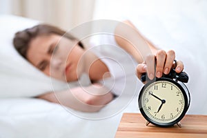 Sleepy young woman stretching hand to ringing alarm willing turn it off. Early wake up, not getting enough sleep concept