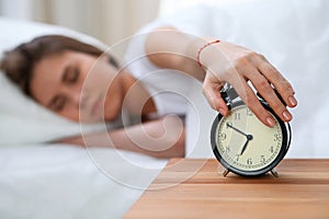 Sleepy young woman stretching hand to ringing alarm willing turn it off. Early wake up, not getting enough sleep concept