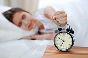 Sleepy young woman stretching hand to ringing alarm willing turn it off. Early wake up, not getting enough sleep concept