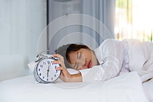 Sleepy young woman stretching hand to trying kill alarm clock in