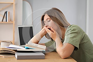 Sleepy young woman studying at wooden table indoors