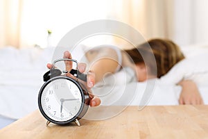 Sleepy young woman trying kill alarm clock