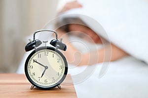 Sleepy young woman under blanket with her head don`t want to wake up in front of alarm clock closeup. Early wake up, not