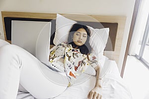 A sleepy young woman yawning while working from the bed