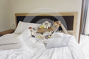 A sleepy young woman yawning while working from the bed