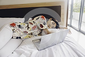 A sleepy young woman yawning while working from the bed