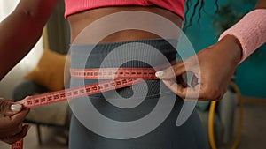 A slender African American woman measures her waist with a measuring tape. Side view of a woman& x27;s thin waist wrapped