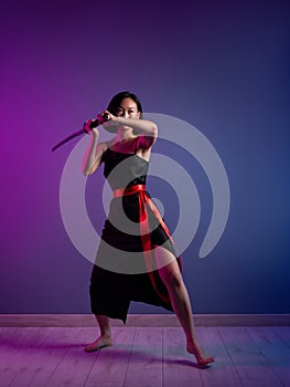 slender Asian woman in a black dress with a katana in her hand image of a samurai on a neon background