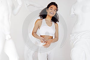 Slender attractive african woman in white sportswear measuring waist using tape