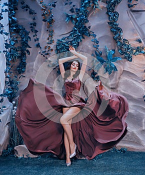 Slender attractive lady like picture of gorgeous artist, flying fluttering marsala long satin dress like paint strokes