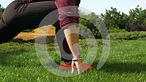 Slender and beautiful young woman in sportswear preparing for workouts on the lawn near her house, doing exercises for warm-ups. Y