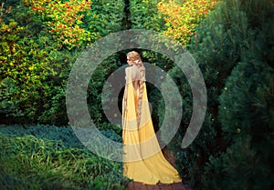 Slender beauty in elegant bright dress with stretching trains goes to thick of magical garden, golden elf princess with