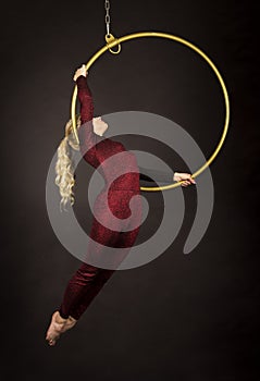 A slender blonde girl-an air acrobat in a red suit with long hair , performs exercises in an air ring