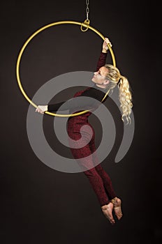 A slender blonde girl-an air acrobat in a red suit with long hair , performs exercises in an air ring