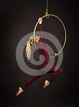 A slender blonde girl-an air acrobat in a red suit with long hair , performs exercises in an air ring