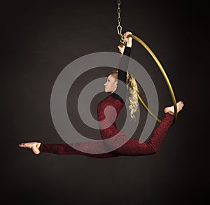 A slender blonde girl-an air acrobat in a red suit with long hair , performs exercises in an air ring