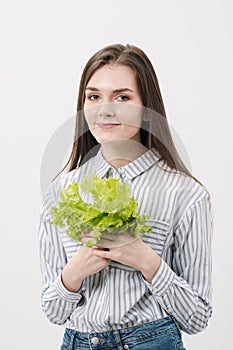 A slender brunette girl with long hair on a white background, holds in her hands and shows the leaves of green fresh