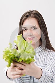 A slender brunette girl with long hair on a white background, holds in her hands and shows the leaves of green fresh