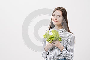 A slender brunette girl with long hair on a white background, holds in her hands and shows the leaves of green fresh