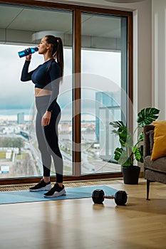 Slender brunette woman drinks water by panoramic window