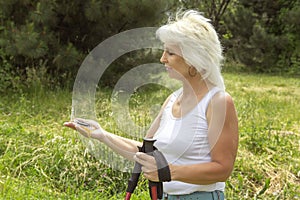 Slender elderly woman with gray hair with a compass in her hands for orienteering and sticks for walking.