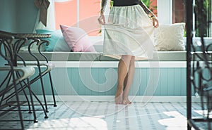 Slender female legs standing on the floor in bright living room. Floor lit by sunlight. Wears a long skirt. Model with