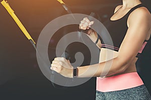 A slender girl holds a strap in her hand for the suspension training in the gym.