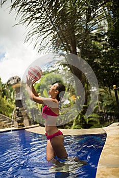 Slender girl model in a sexy pink swimsuit plays ball in a tropical pool in the jungle