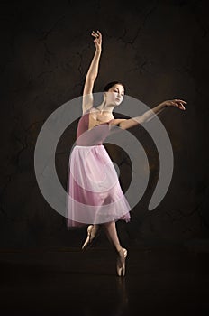 A slender girl in a pink skirt and beige top dancing ballet