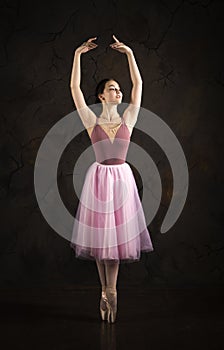 A slender girl in a pink skirt and beige top dancing ballet