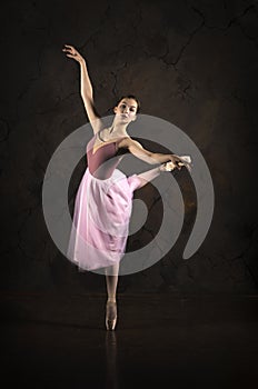 A slender girl in a pink skirt and beige top dancing ballet