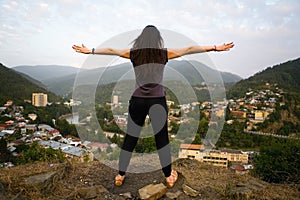 The slender girl raised her hands in different directions against the background of Borjomi.