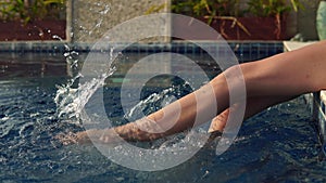 Slender girl sunbathes and dangles her legs in pool