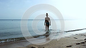 A slender girl in a swimsuit slowly enters a calm sea and then floats. Clear blue sky and water without waves.