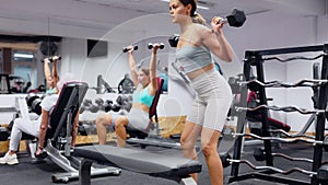 Slender girl trains muscles of arms and back using barbell and differentiated weighting in gym