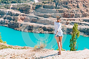 A slender girl in a white shirt dancing alone by the sandy career. Against the background of mountains and a blue azure lake.