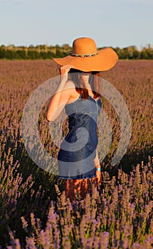 slender girls with jeans dress holding straw hat in the middle of the field at sunset